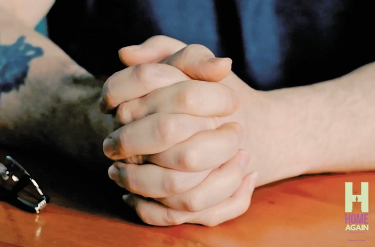 man's hands resting on a wooden table