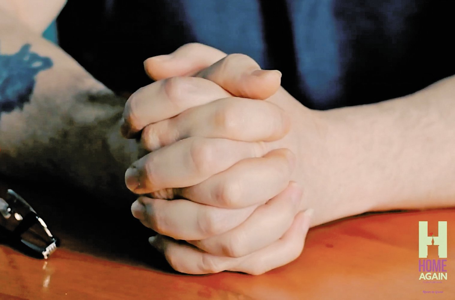 man's hands resting on a wooden table
