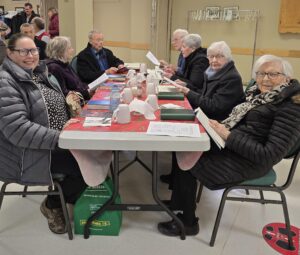 people attending a church service in a parish hall, with coats on, sitting around a folding table