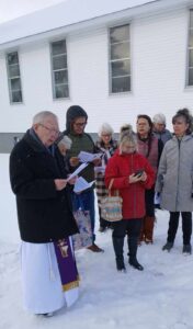 a man dressed as an Anglican priest stands outside with a number of other people to bless a new columbarium 