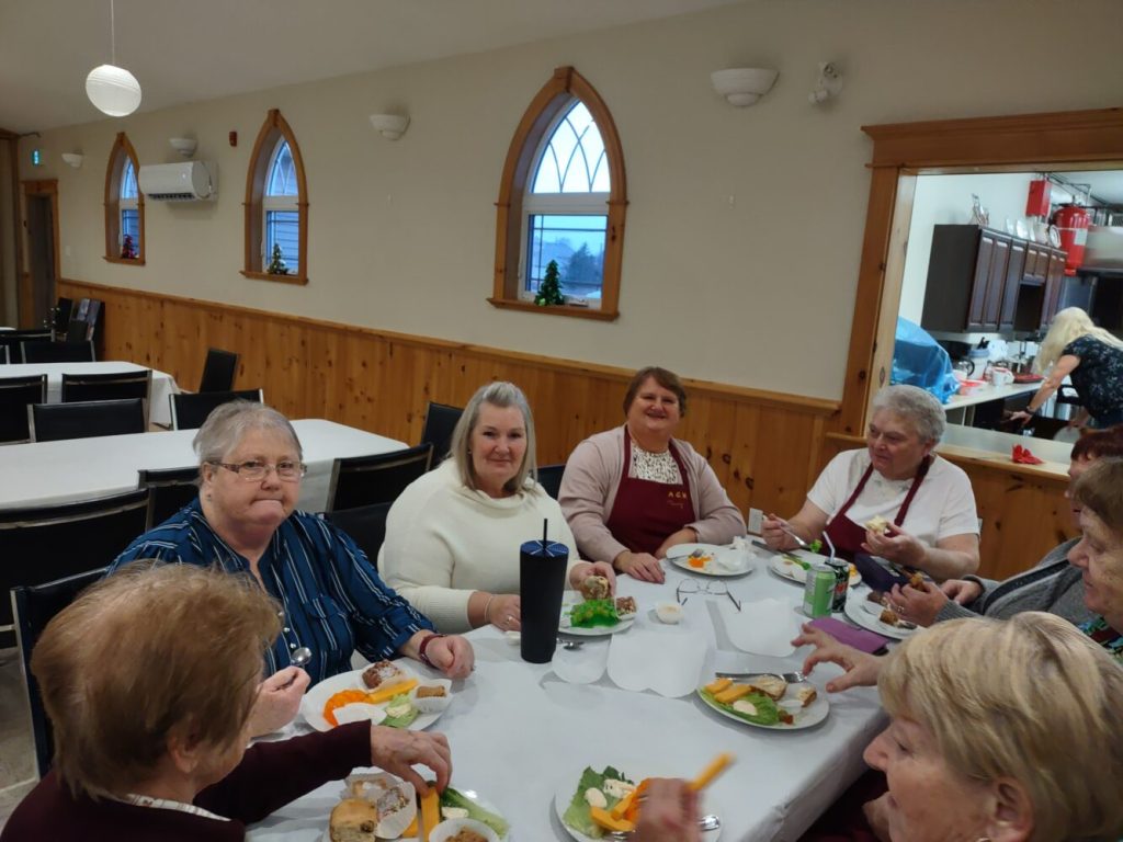 people sitting around a folding table in a parish hall during a fall sale