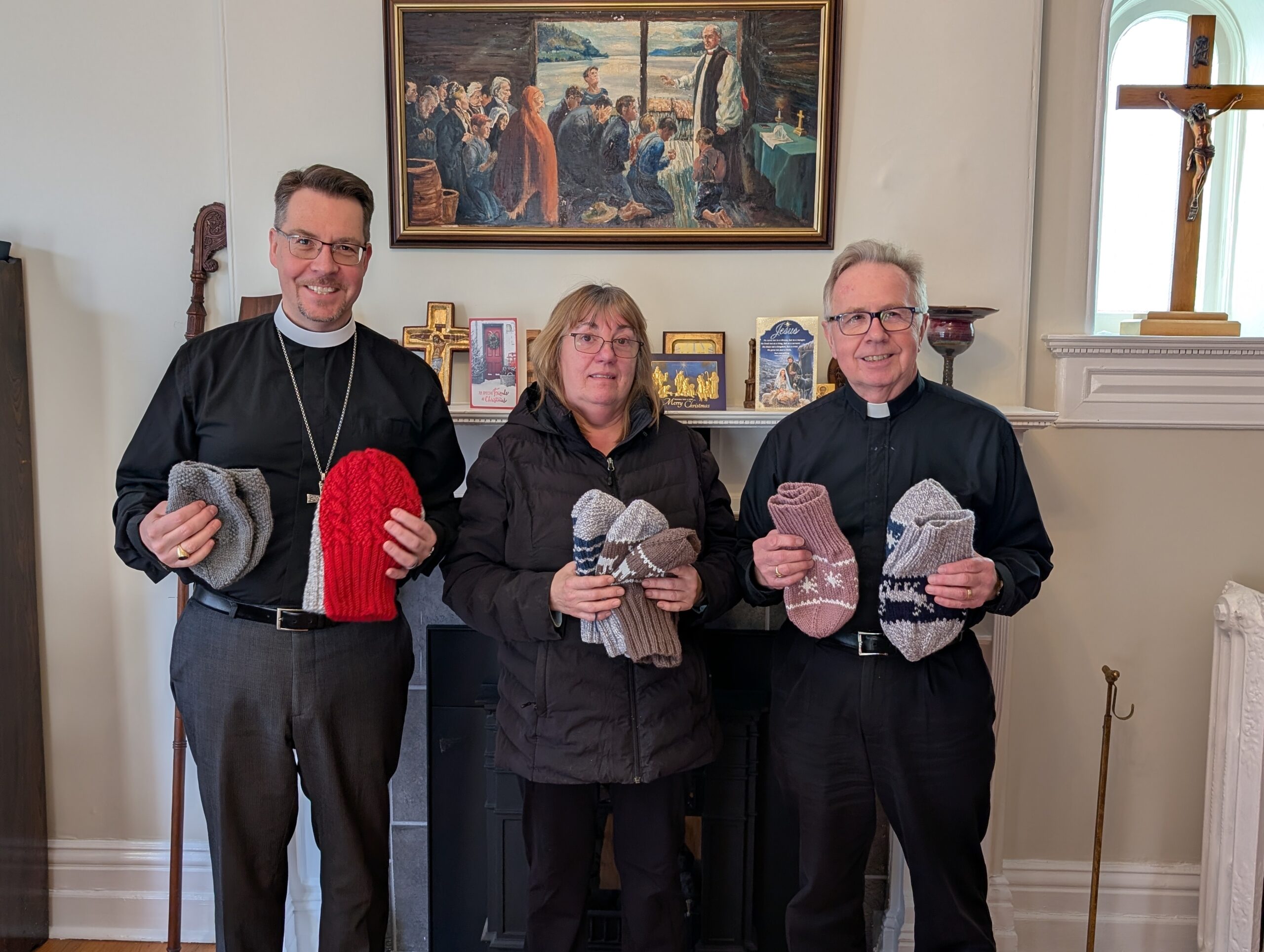 three people hold knitted goods that have been made as donations for those in need