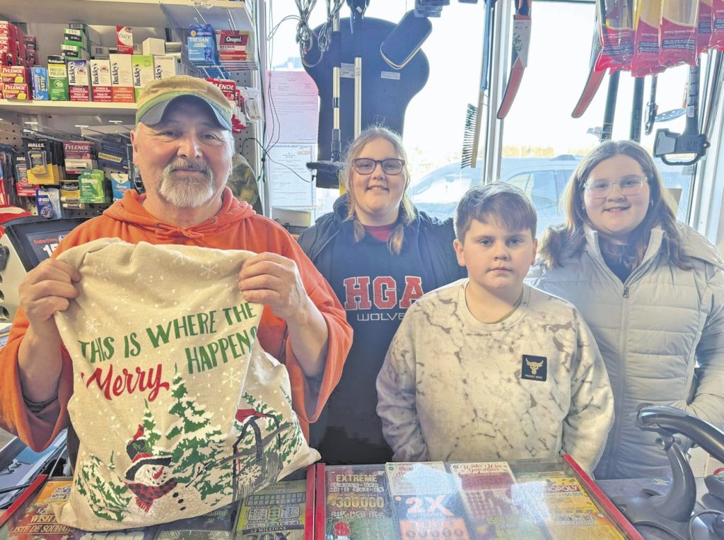 four people stand behind the counter in a store with a bag of Christmas gifts