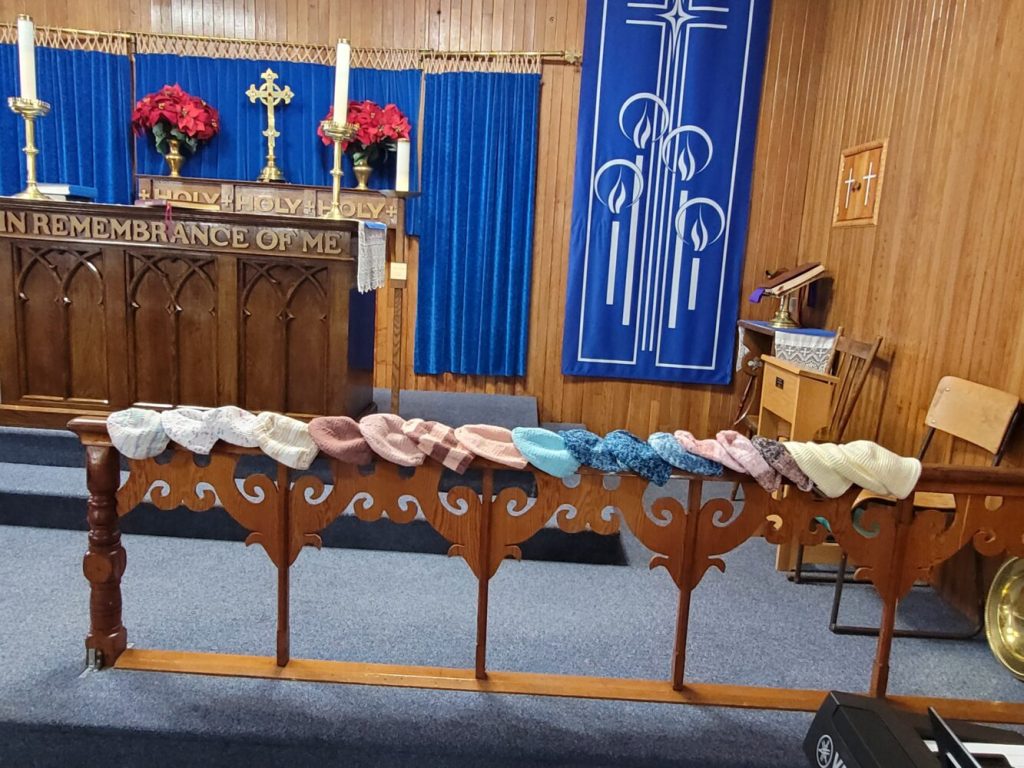 knitted and crocheted caps, made for chemo patients, lined up along a communion rail in a church