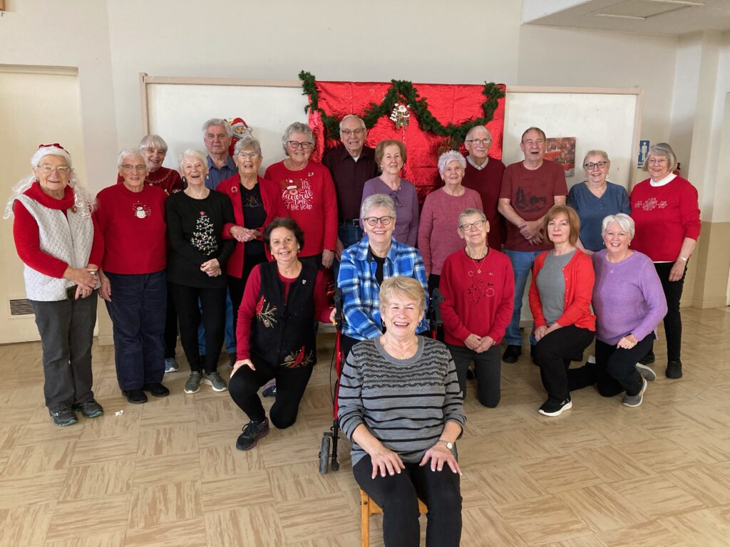 a group of older people, some standing and some sitting on chairs, who are part of an exercise group at a local church