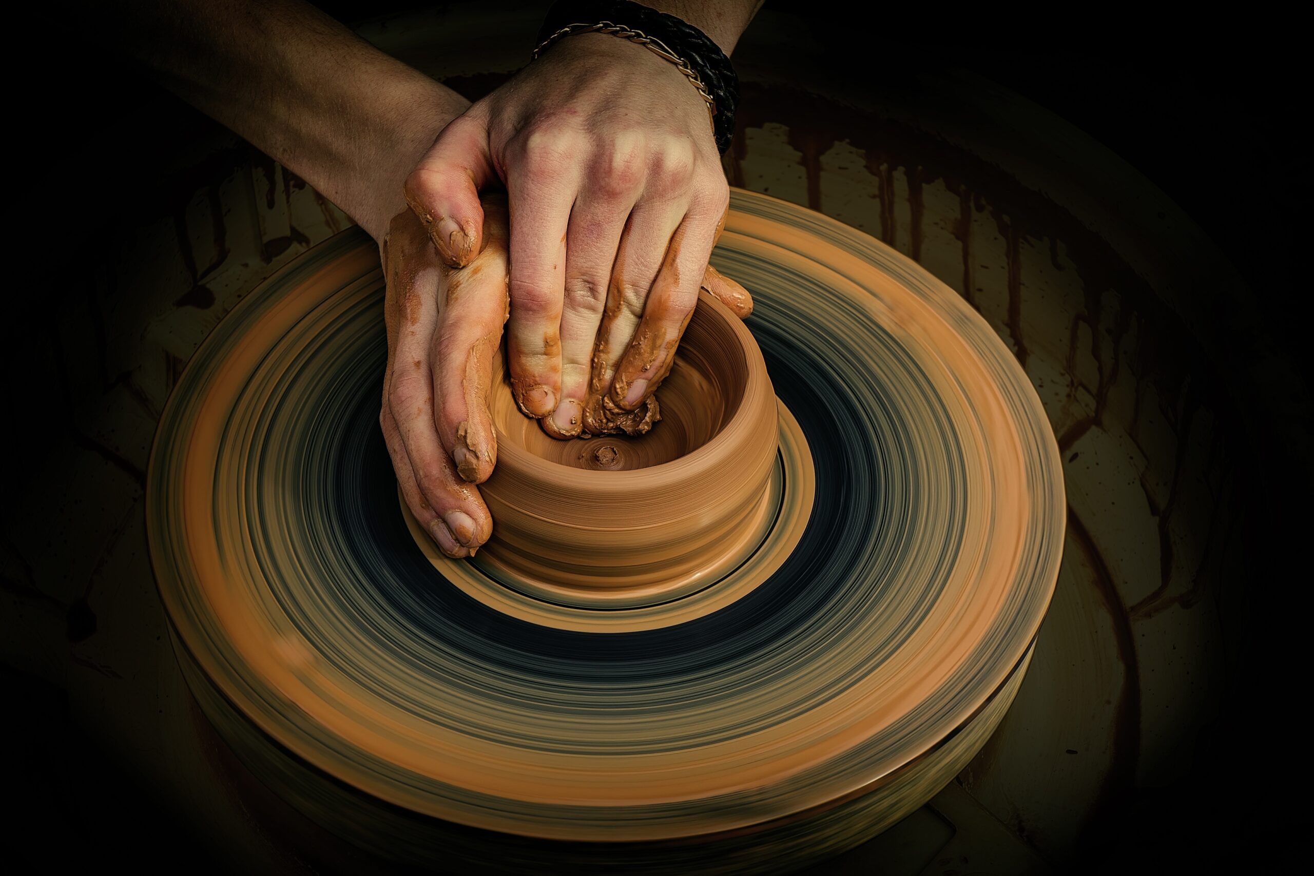 two hands work to shape a clay pot on a pottery wheel