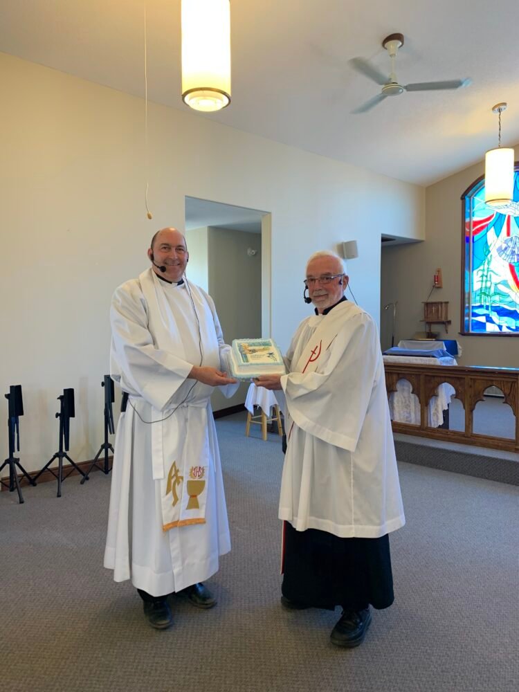 two members of the Anglican clergy pose for a photograph with a cake in a church
