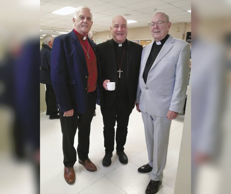 Three men, all dressed as members of the Anglican clergy, smile for a photograph