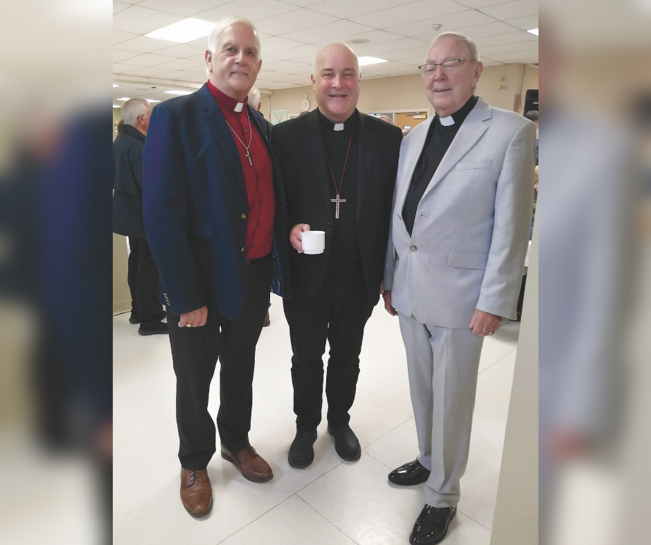 Three men, all dressed as members of the Anglican clergy, smile for a photograph