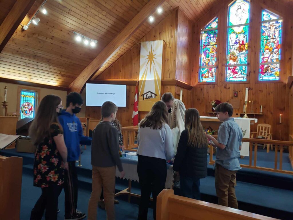 a group of young people gather at the front of a church with a priest to see a Christingle