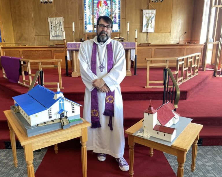 an Anglican priest between two modesl of churches that he has built from Lego