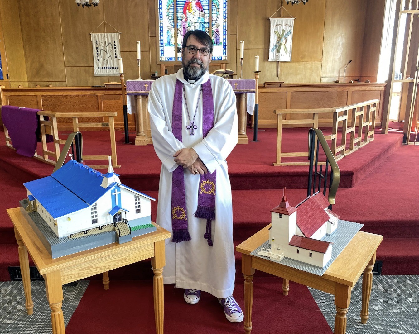 an Anglican priest between two modesl of churches that he has built from Lego
