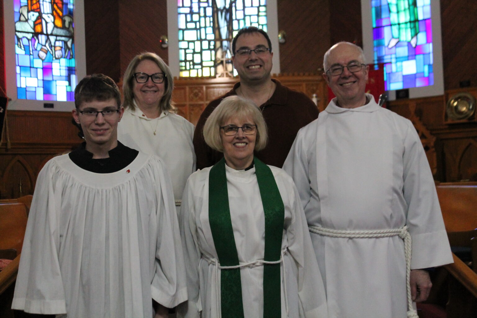 five people, four adults and one child, at the front of a church; all but one of the adults is dressed in church vestments of some kind