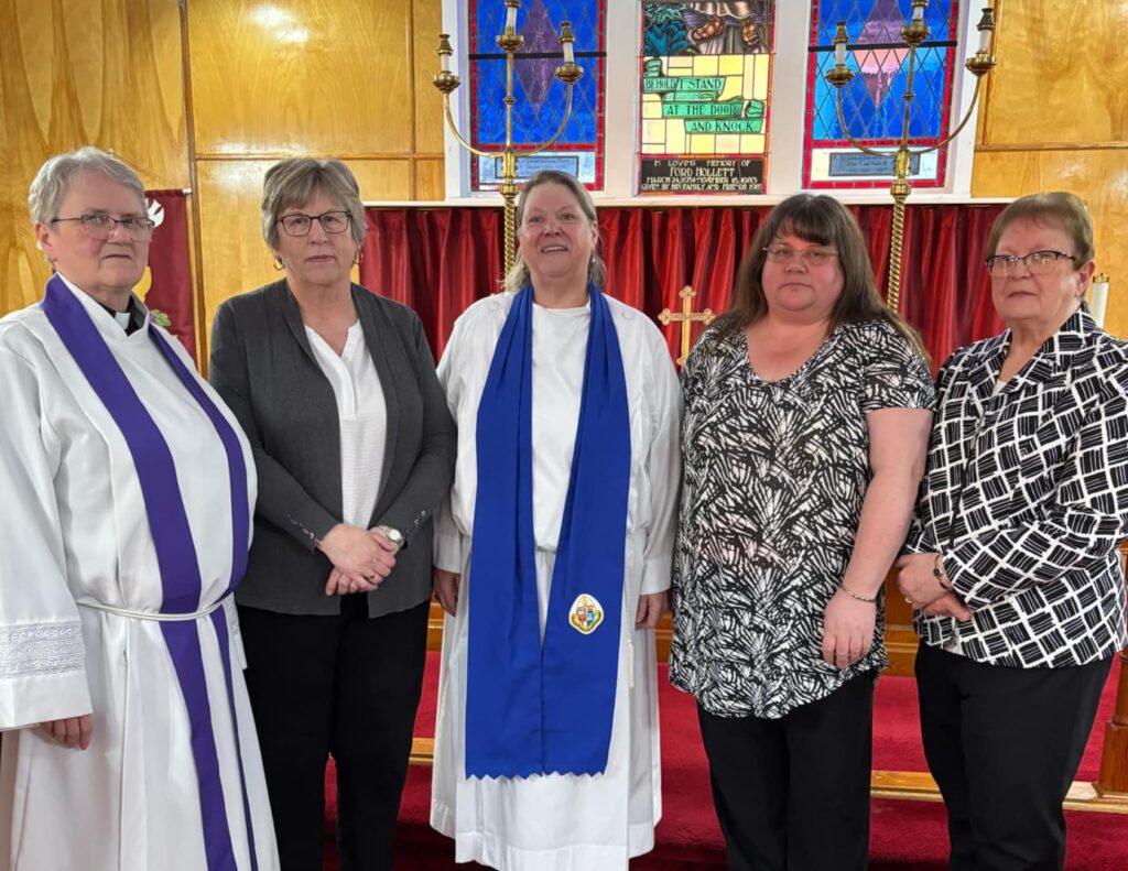 a group of 5 women stand at the front of a church, two dressed in church vestments
