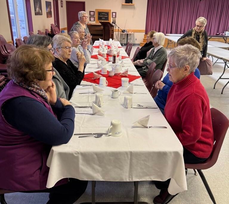 women sitting at a table, set up for a meal, in a church hall