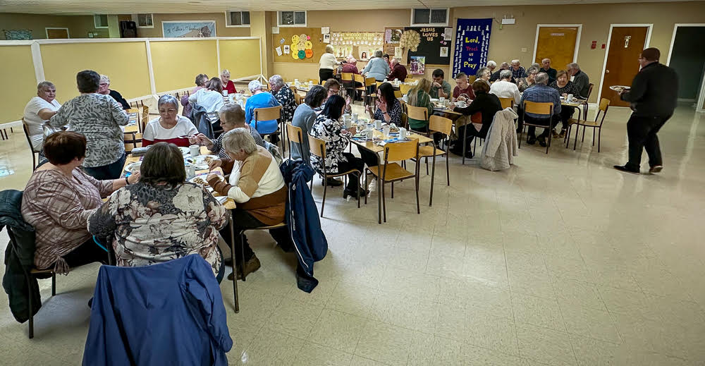 people around long tables in a church hall, enjoying a rice supper