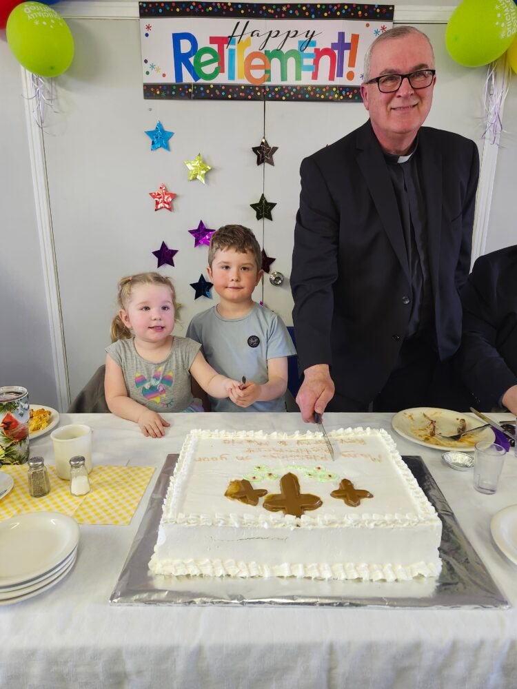 two children and a man dressed as a priest cuts a cake