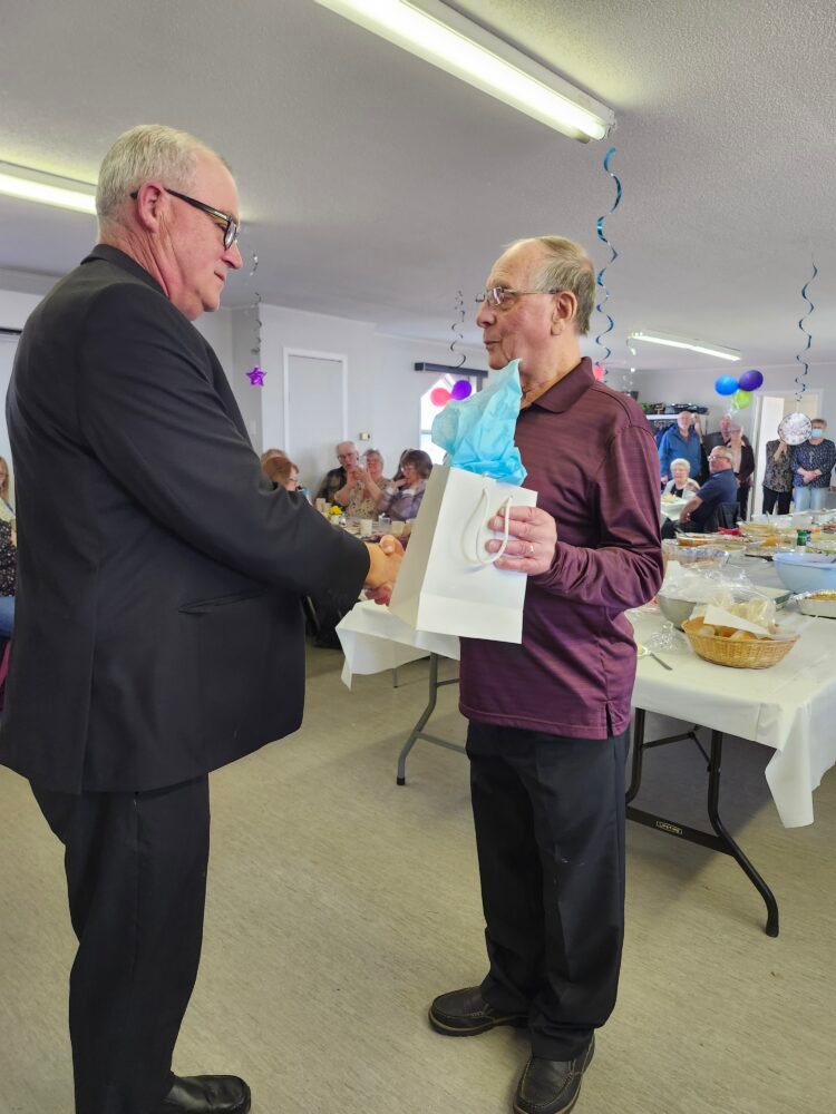 one man presenting a gift to another man, the latter of whom is dressed as an Anglican priest