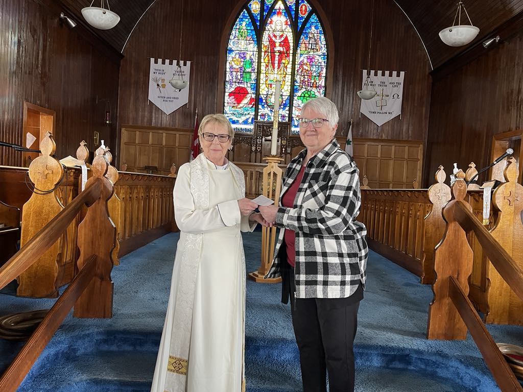 one woman presents a cheque to another woman at the front of a church