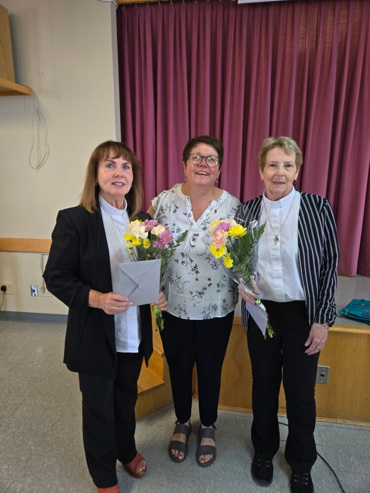 three women, one presenting the other two with flowers