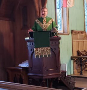 a man, dressed in green vestments, preaching from an old wooden pulpit