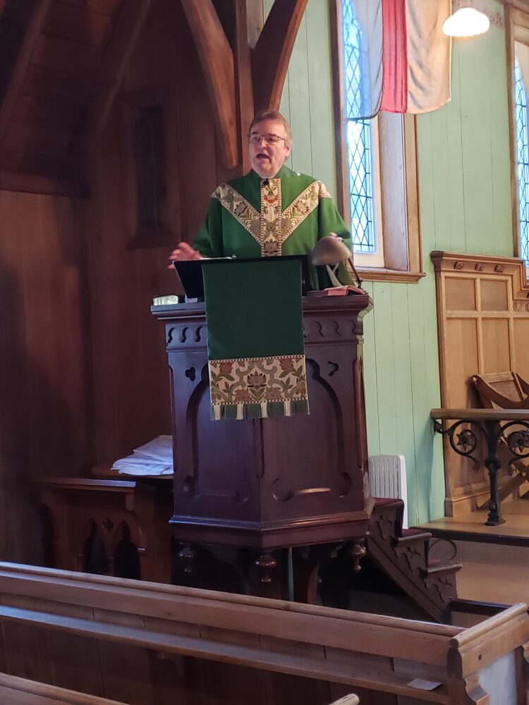 a man, dressed in green vestments, preaching from an old wooden pulpit