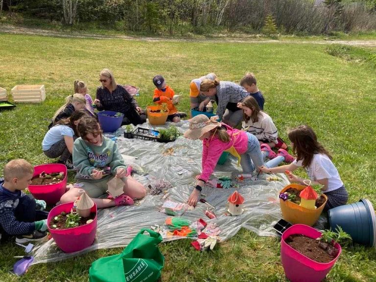 A group of adults and children are on a plastic sheet outside on a grassy lawn.
