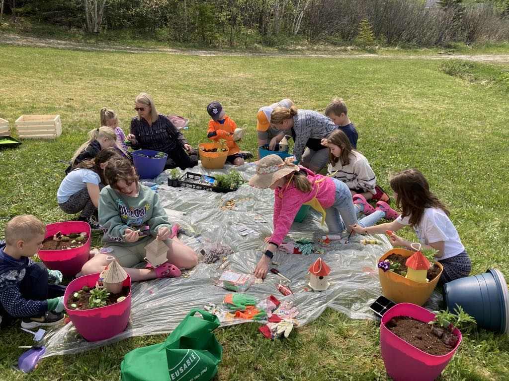 A group of adults and children are on a plastic sheet outside on a grassy lawn.