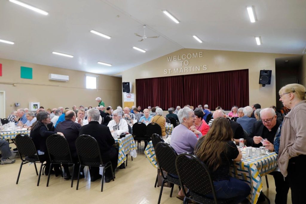 people gathered together for church meetings, sitting around many tables in a parish hall