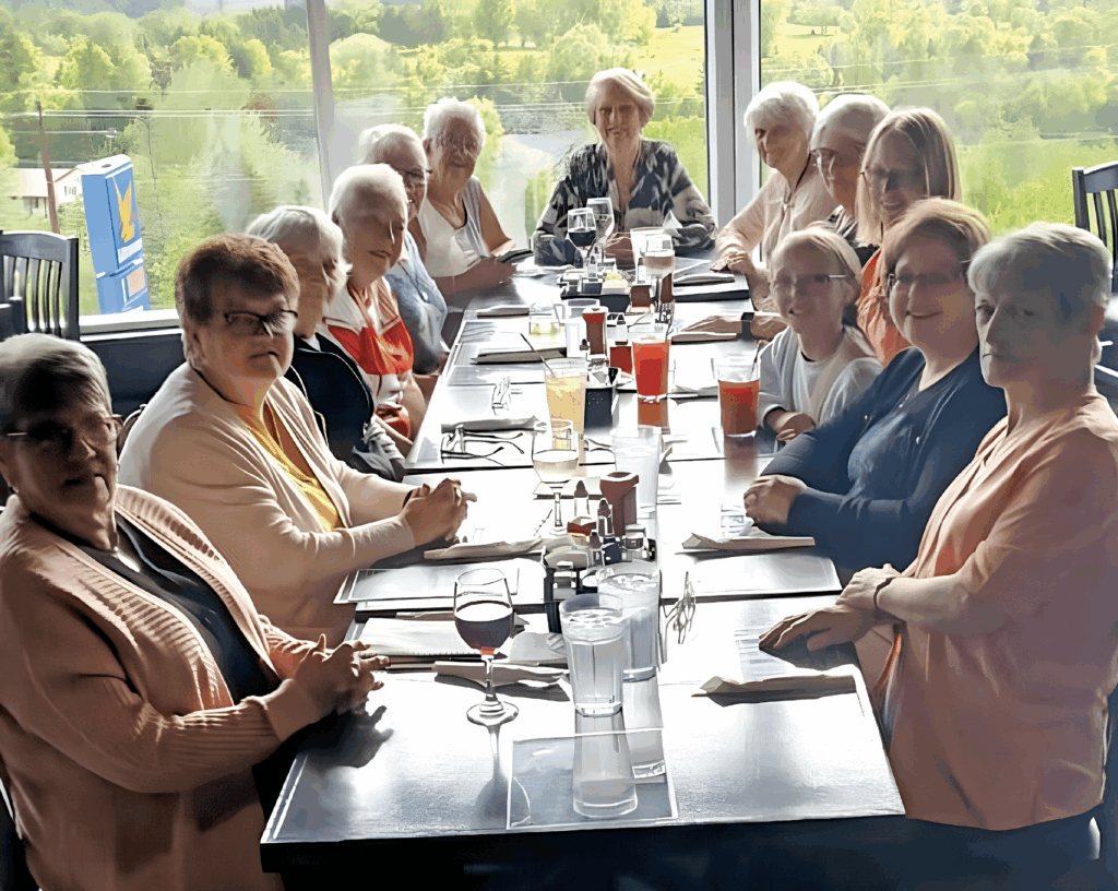 a large group of women, sitting around a table in a restaurant with a window behind them