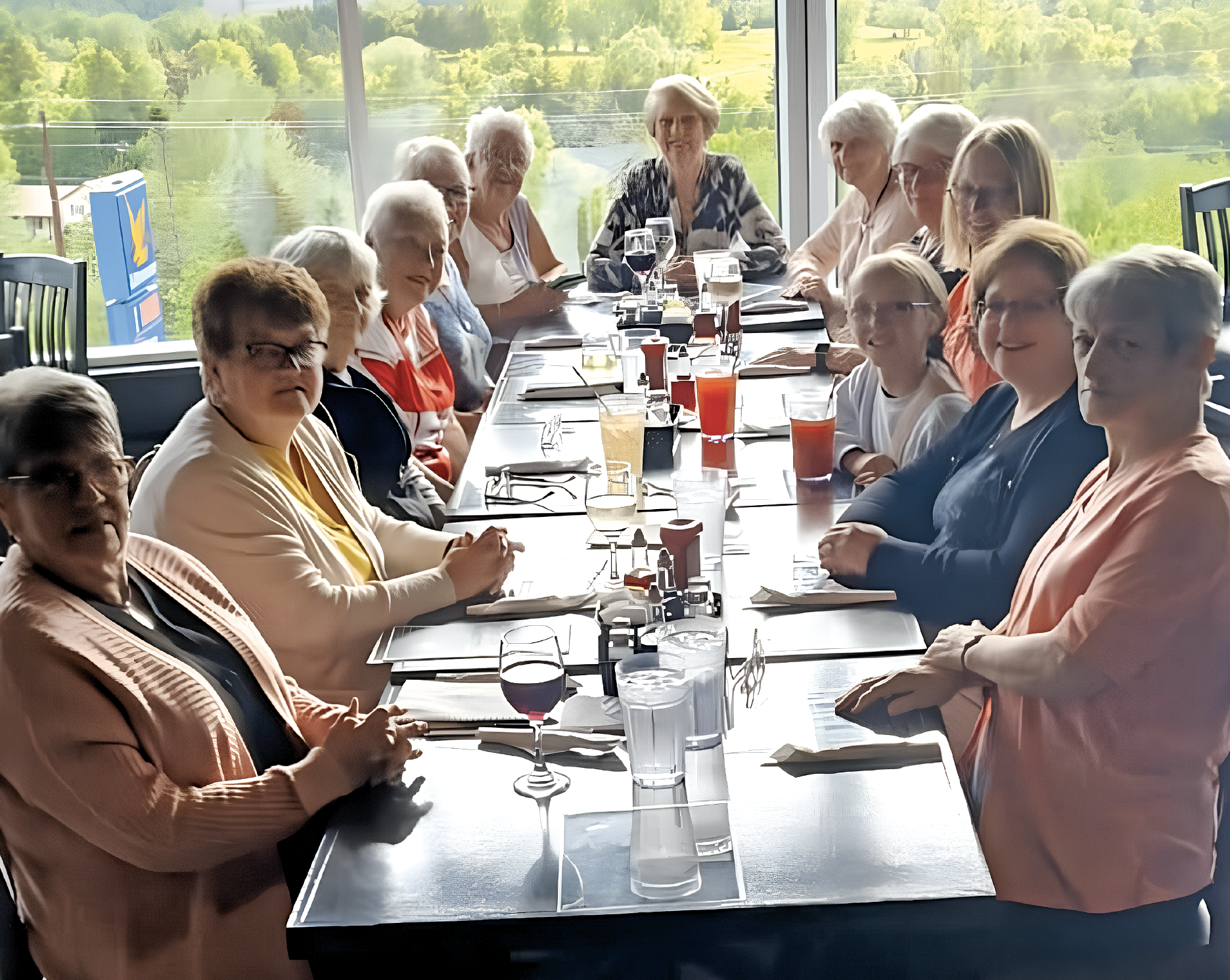 a large group of women, sitting around a table in a restaurant with a window behind them