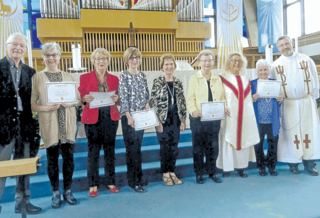 A group of nine people holding certificates inside a church; some are dressed as members of the clergy