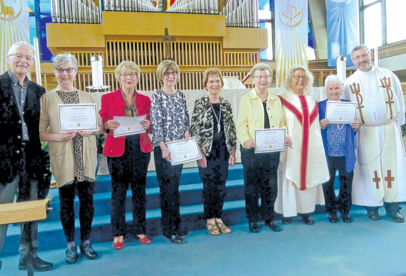 A group of nine people holding certificates inside a church; some are dressed as members of the clergy