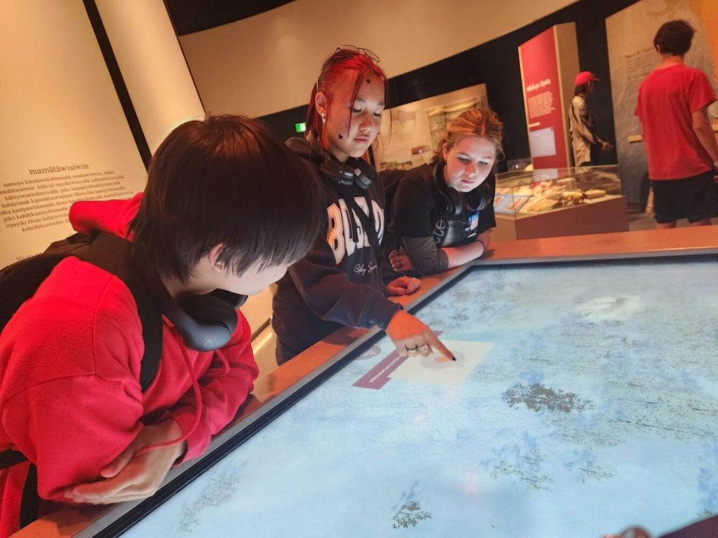 three young people at a museum poiting at an illuminated display