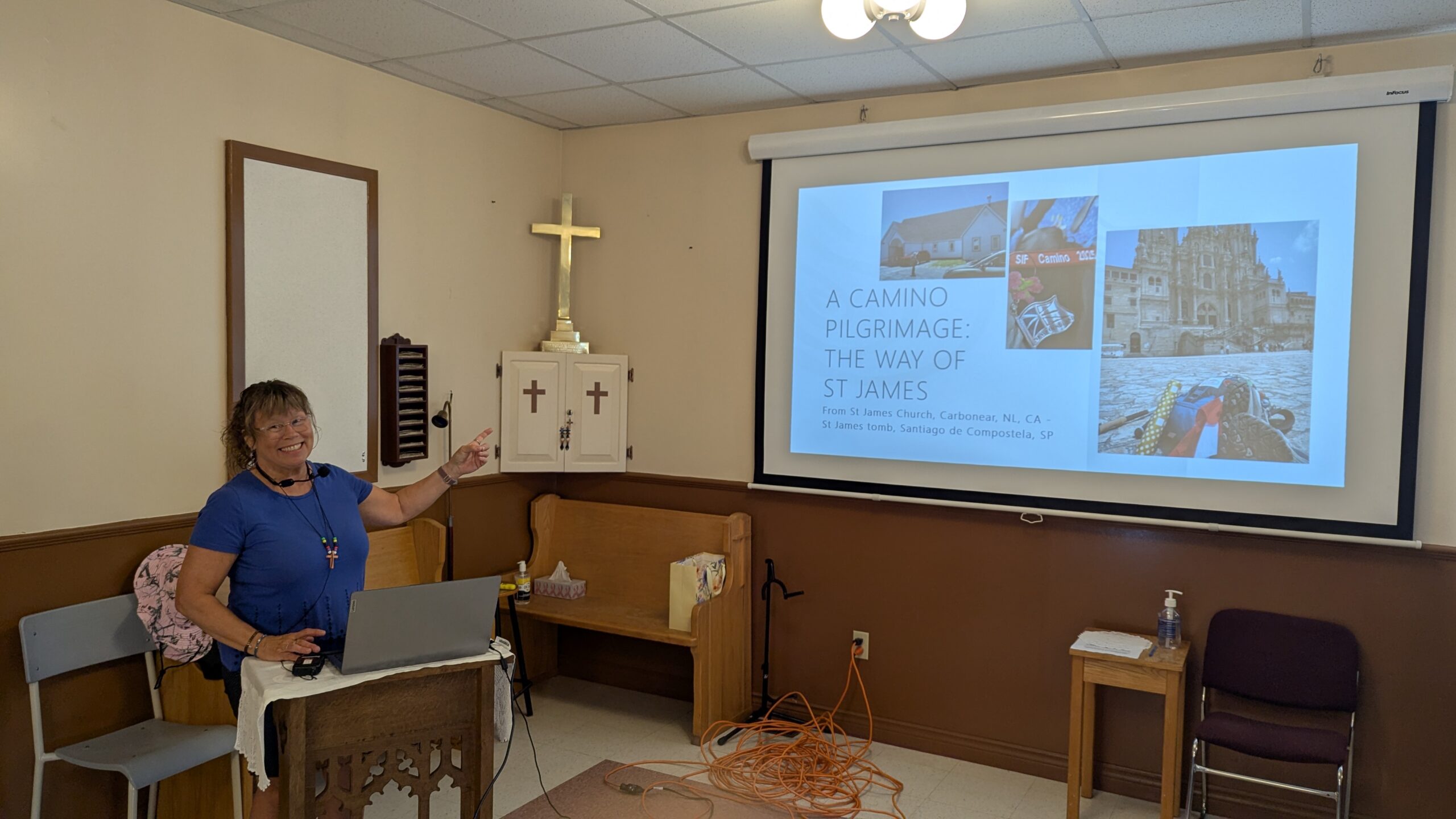 a woman points at a screen where her presentation about her recent pilgrimage to Spain is displayed