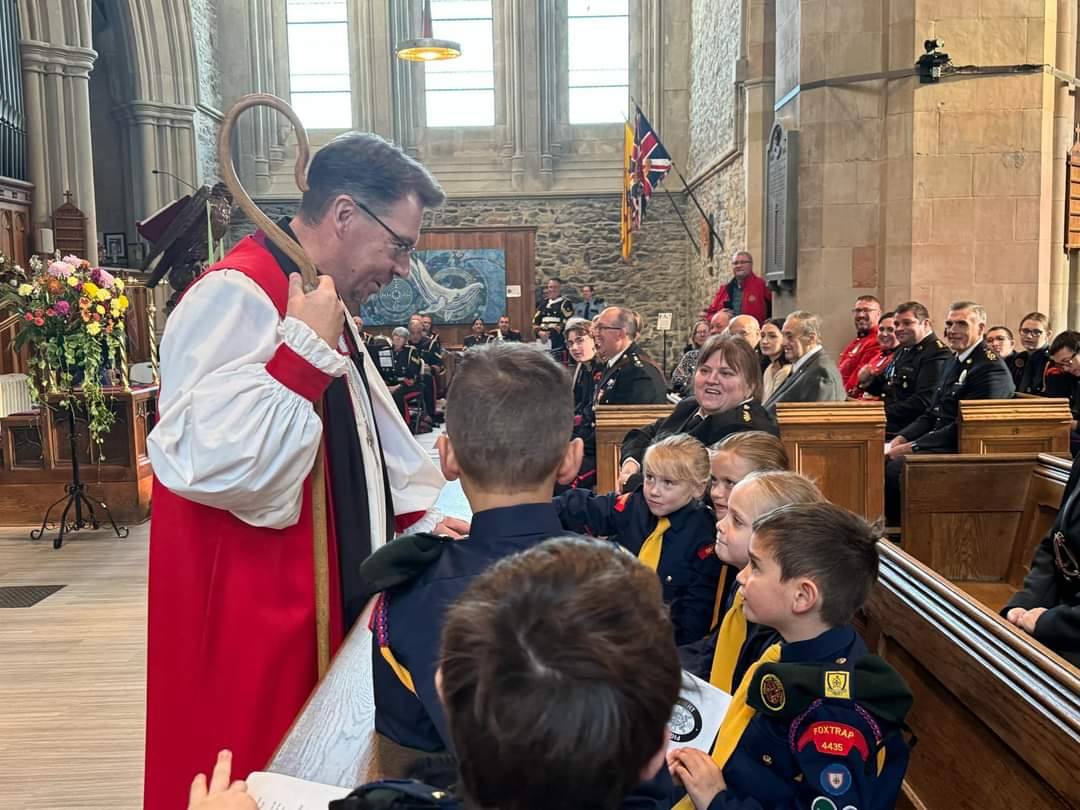An Anglican bishop speaks to a gathered group of youg people dressed in uniforms in a cathedral