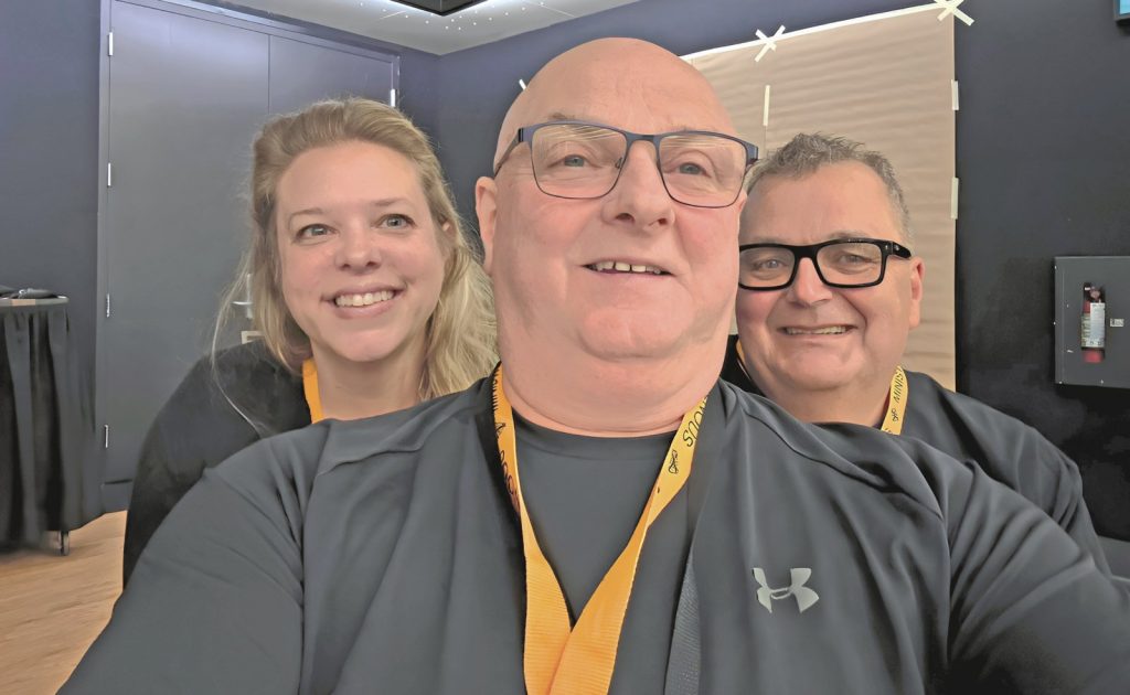 Three people wearing back shirts and orange lanyards