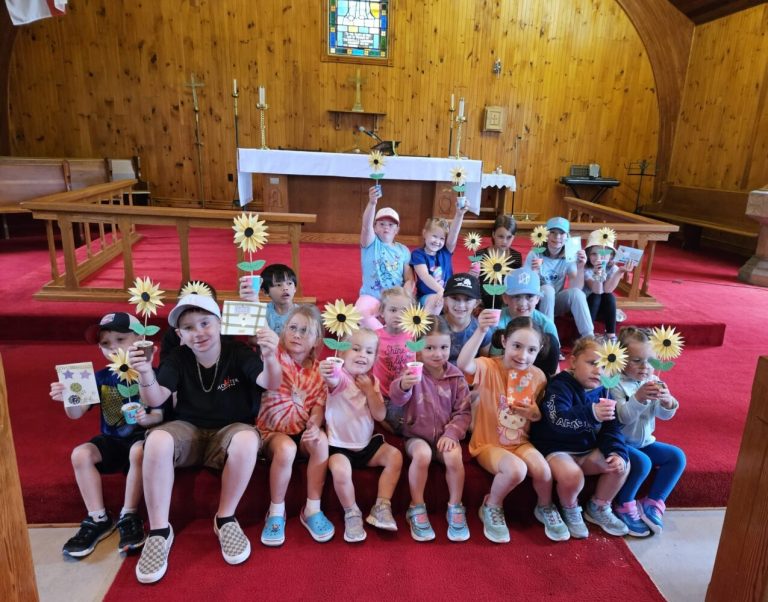 children holding sunflowers while sitting on the floor in front of an altar in a wooden church