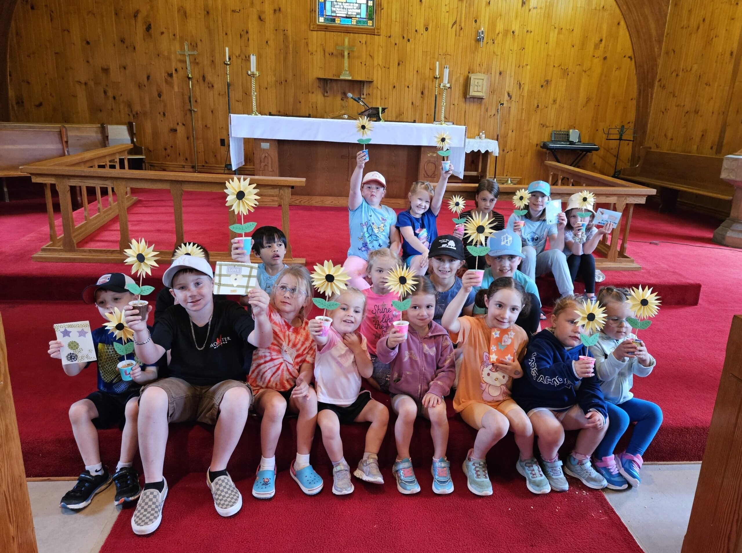 children holding sunflowers while sitting on the floor in front of an altar in a wooden church