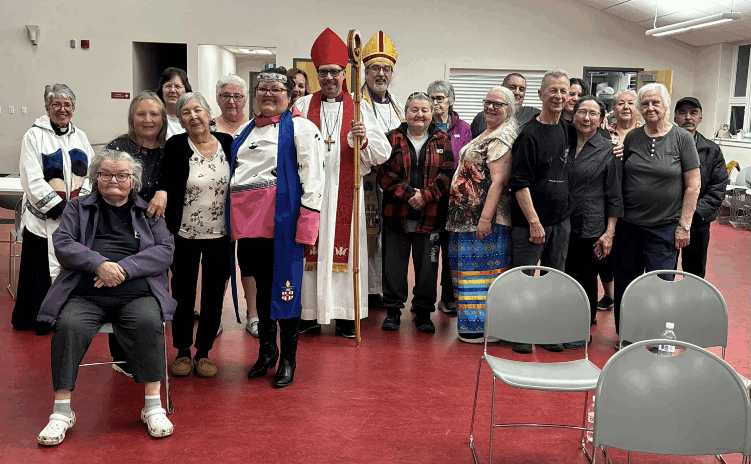 A large group of people, including some wearing clerical vestments, pose for a group photo indoors.