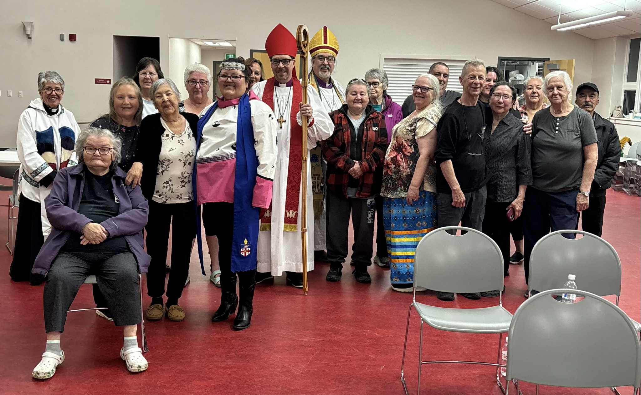 A large group of people, including some wearing clerical vestments, pose for a group photo indoors.