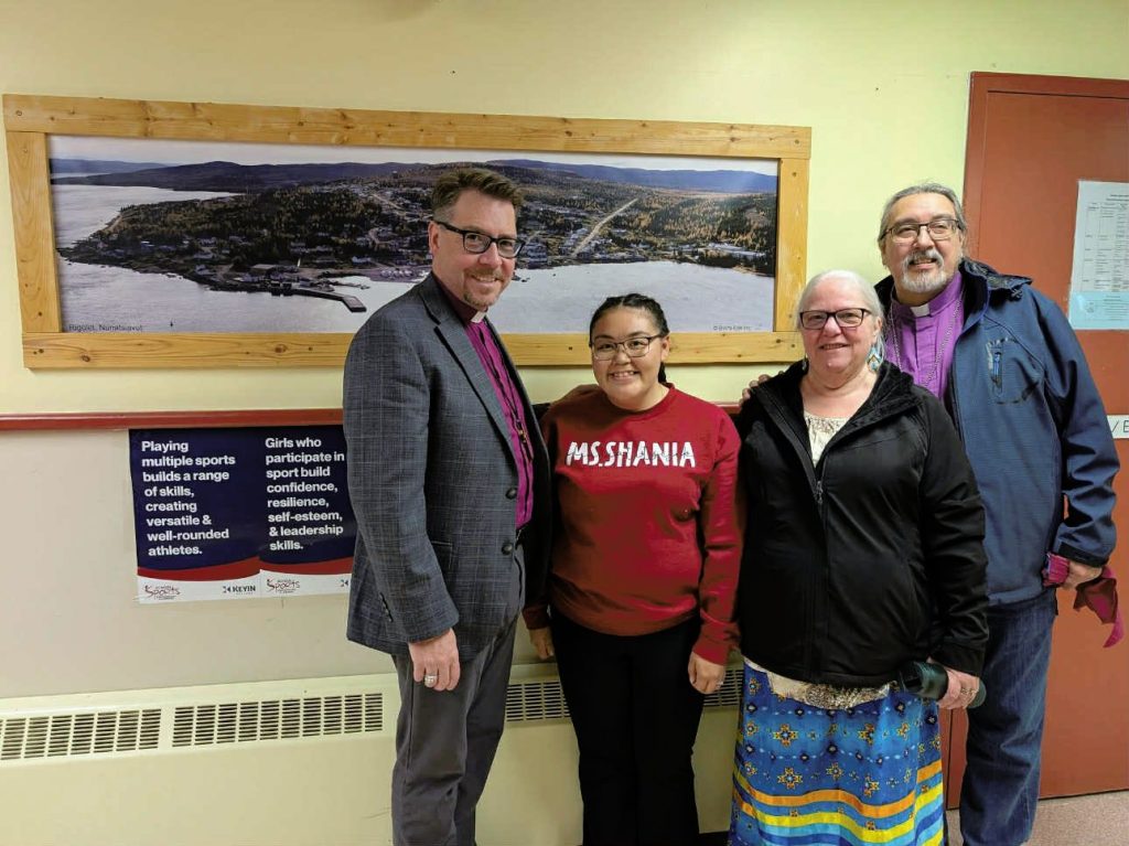 Two men and two women stand smiling for a photo in front of a framed scenic photo.