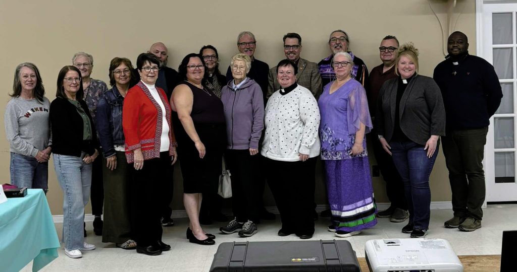 A large group of people, some wearing clerical collars, pose for a group photo indoors.