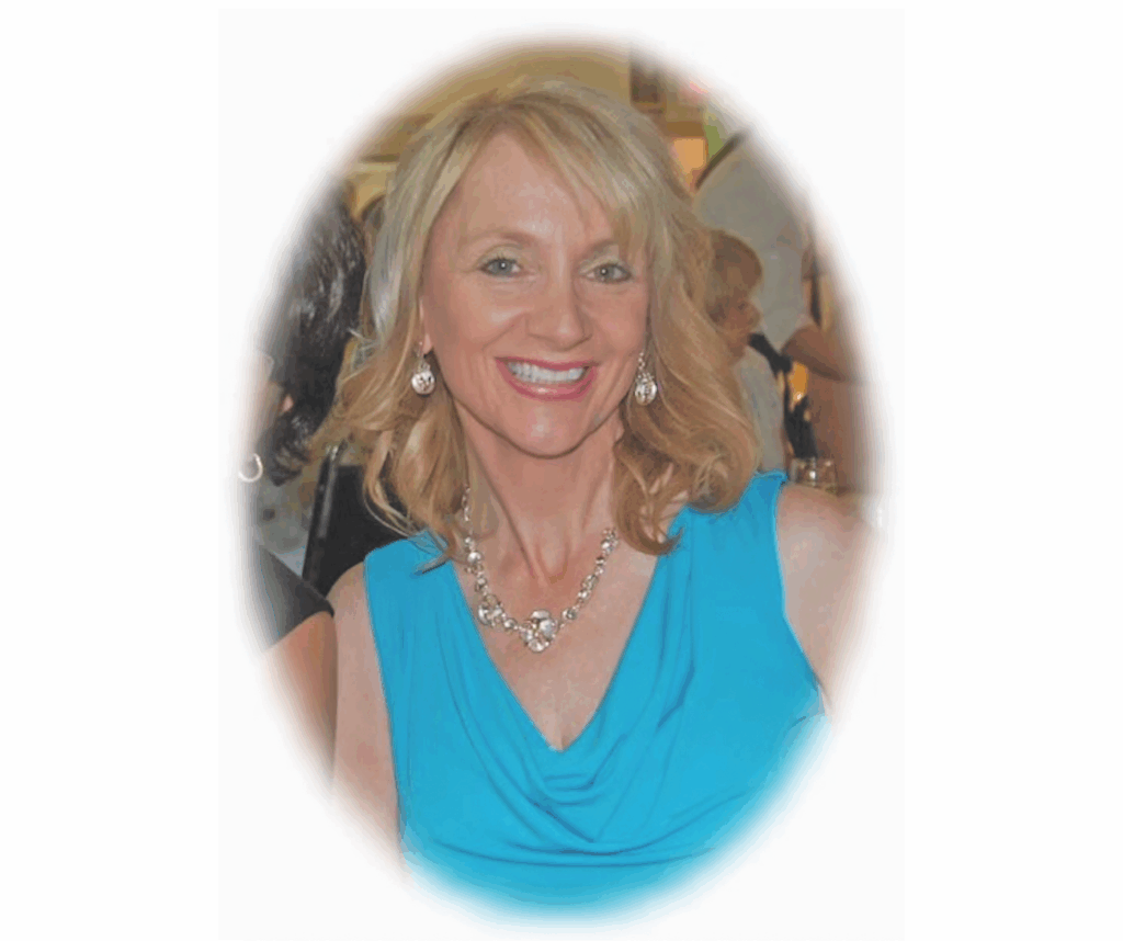 A woman in a blue dress with blonde hair. She is smiling at the camera