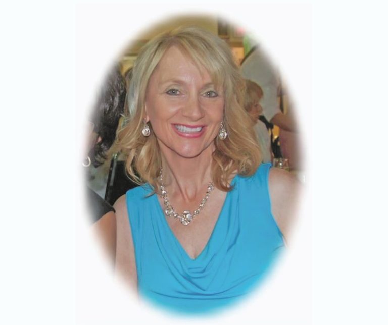 A woman in a blue dress with blonde hair. She is smiling at the camera