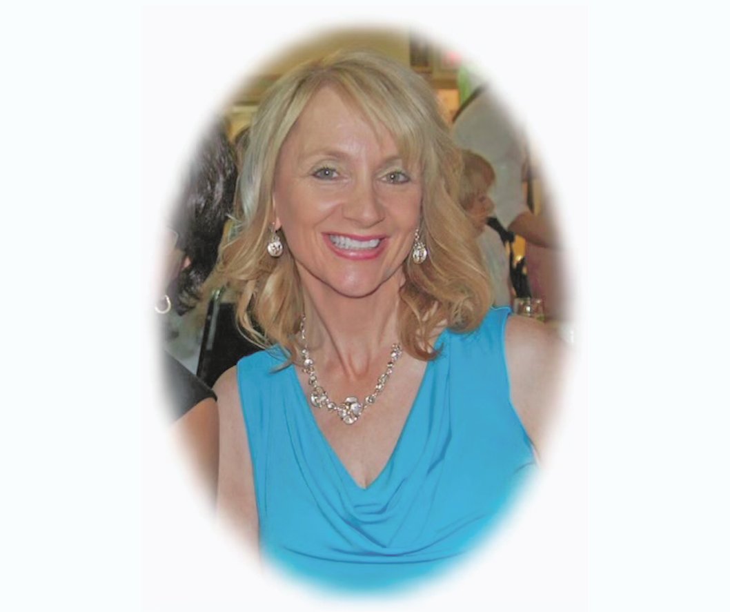 A woman in a blue dress with blonde hair. She is smiling at the camera