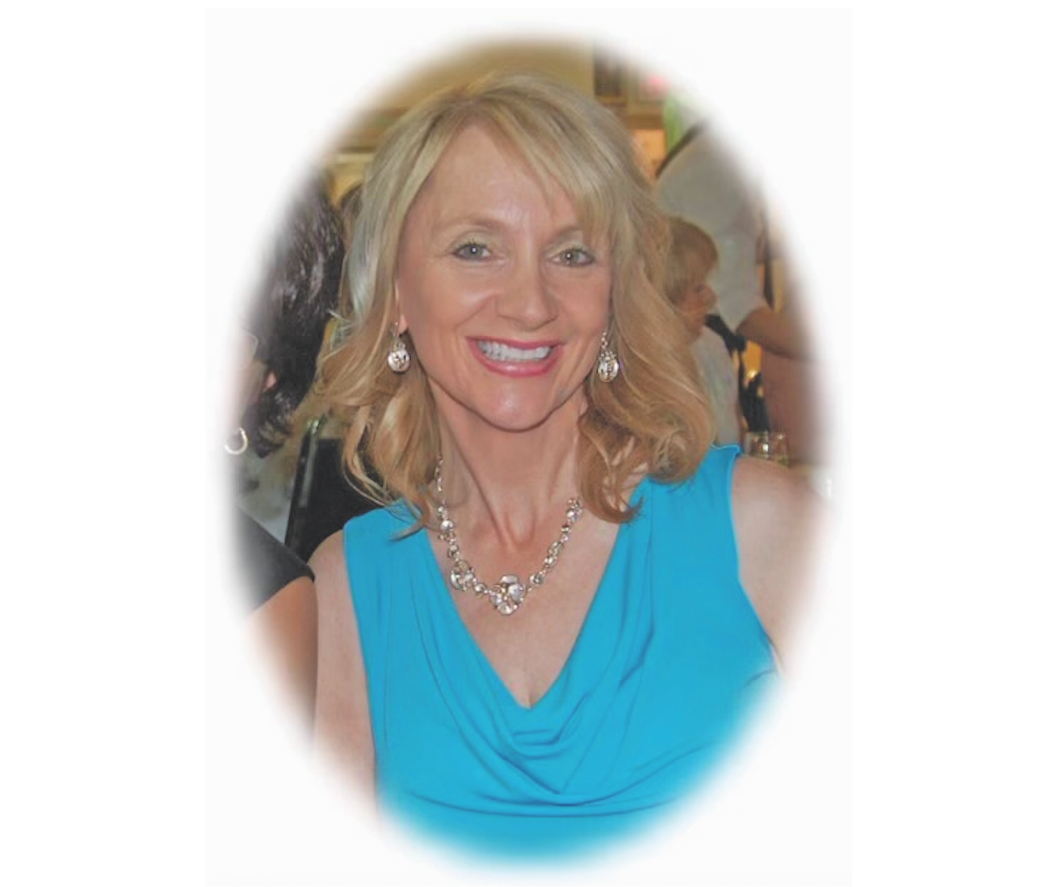 A woman in a blue dress with blonde hair. She is smiling at the camera