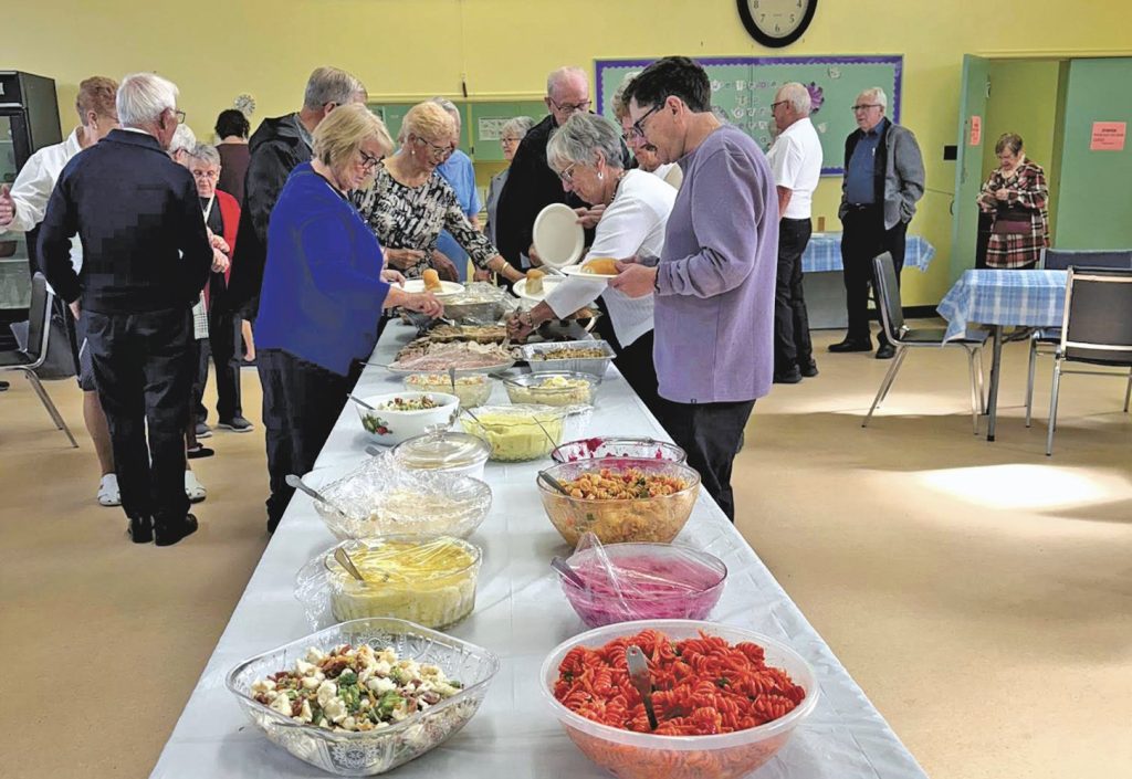 people getting food from a long table at a potluck supper