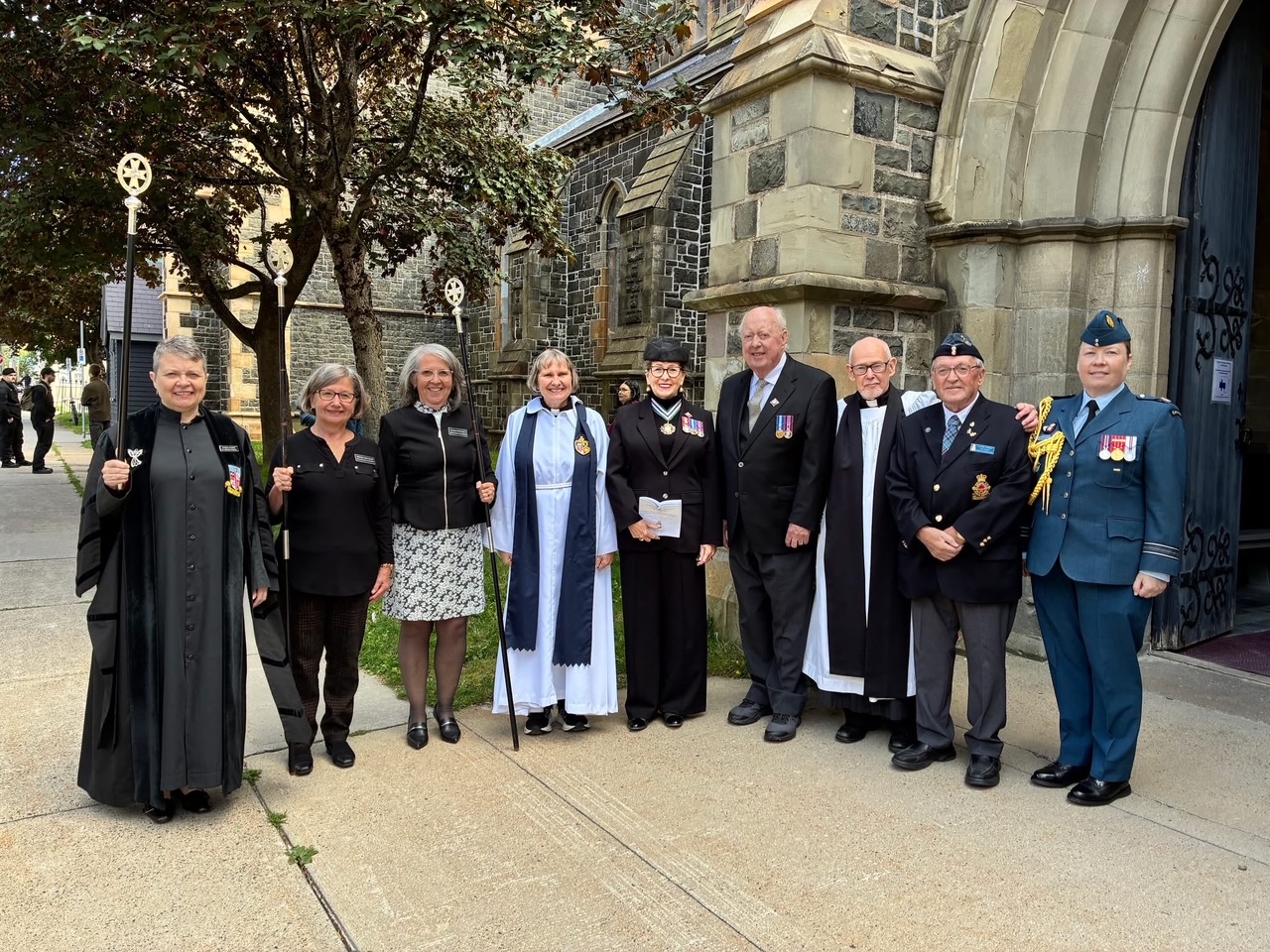 Group of people, some in vestments and military uniform, standing outside a church.