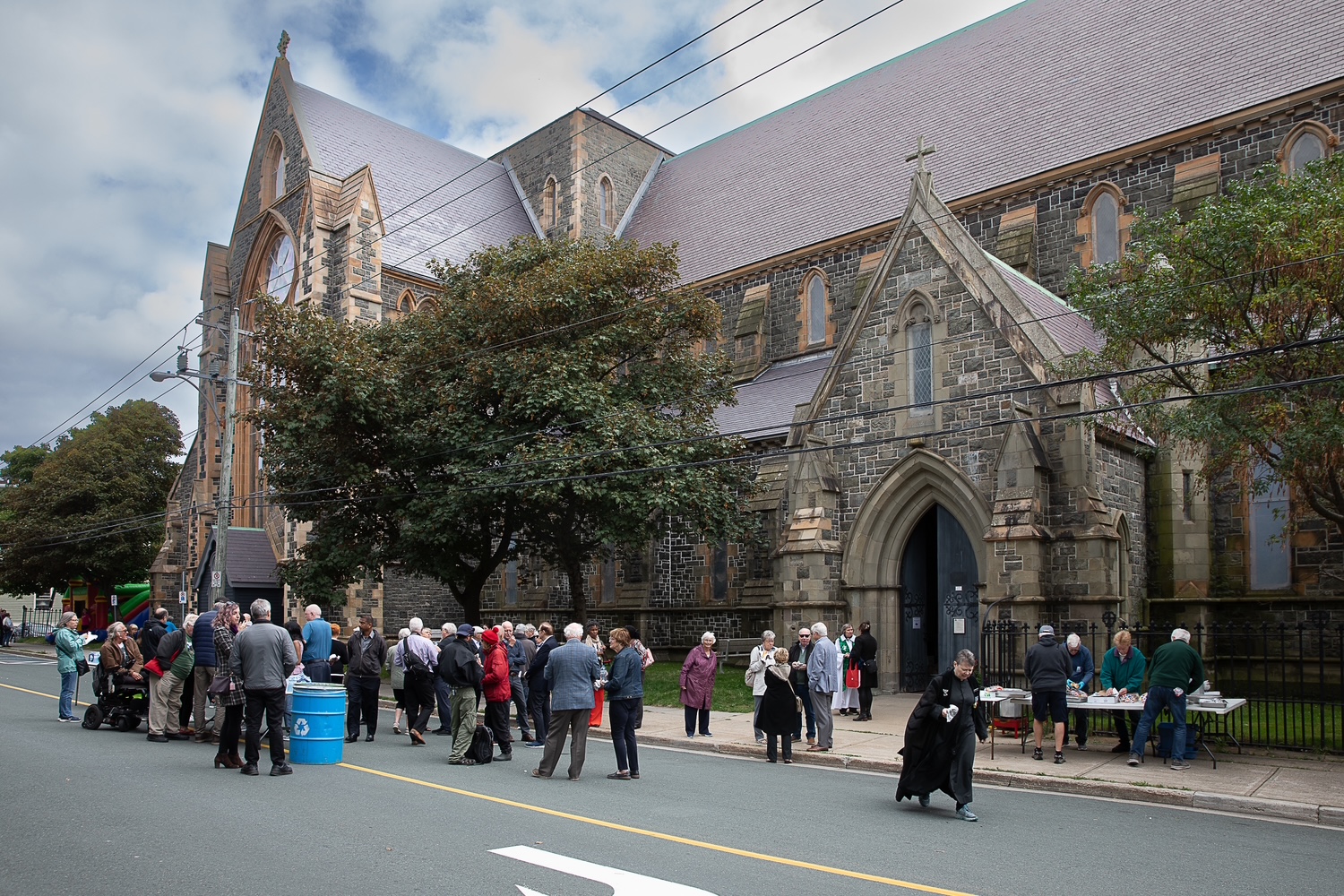 Crowd gathered outside a large, grey stone Gothic Revival church on an overcast day.